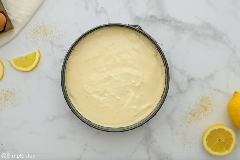Overhead of lemon cheesecake in a springform pan with lemons sitting beside