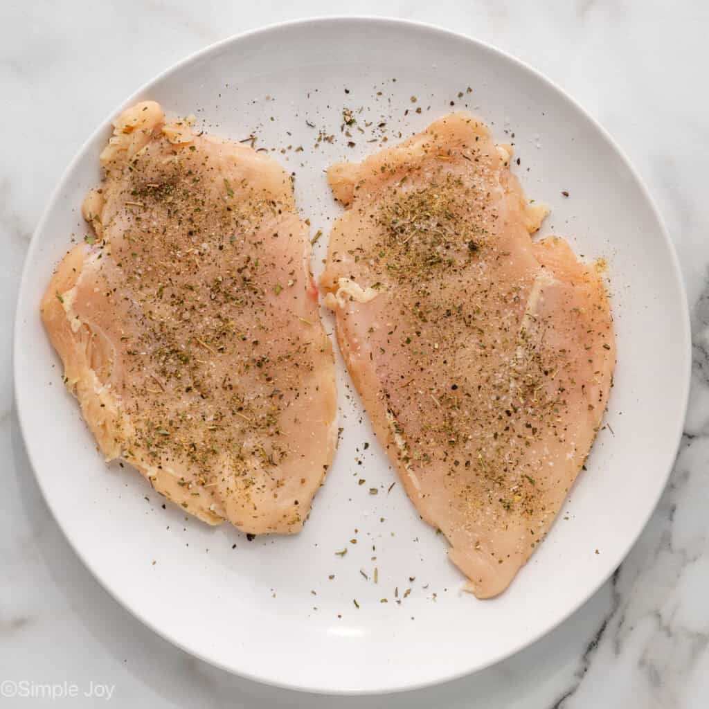 Overhead of seasoning chicken breasts on a plate to make One Pot Lemon Chicken and Orzo