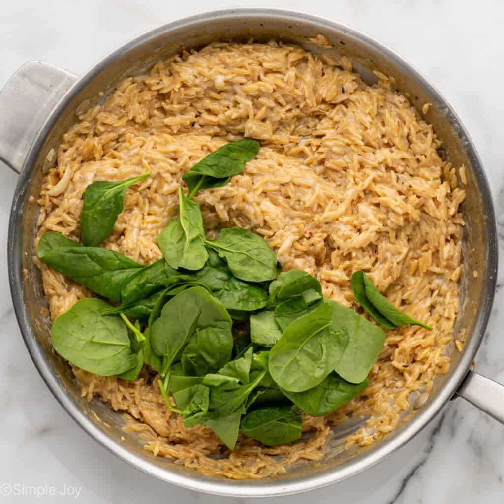 Overhead of skillet of One Pot Lemon Chicken and Orzo ingredients with spinach leaves