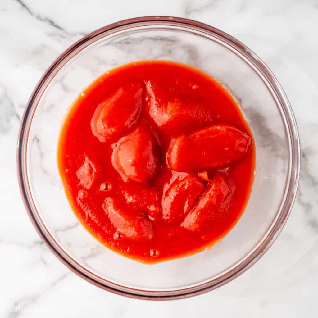 Overhead of glass bowl of tomatoes and tomato juice to make Pasta Puttanesca