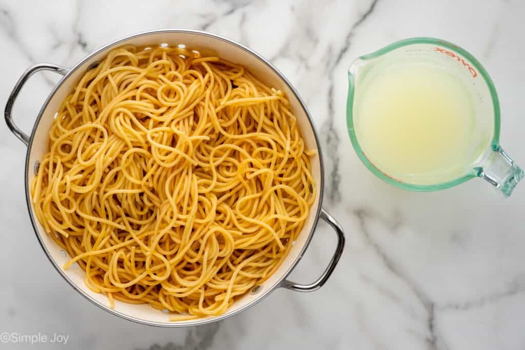 Overhead of colander of cooked spaghetti with glass measuring cup of pasta water sitting beside
