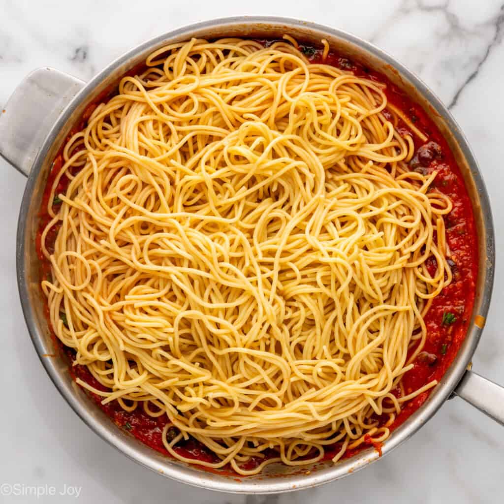 Overhead of Pasta Puttanesca ingredients topped with cooked spaghetti