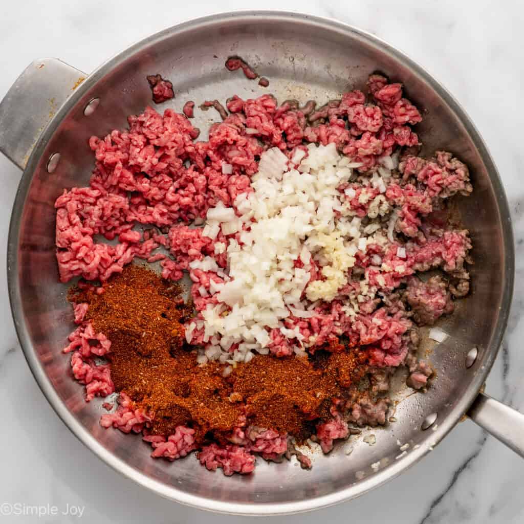 Overhead of skillet of ground beef, diced onion, garlic, and seasonings to make One Pan Cheesy Taco Pasta
