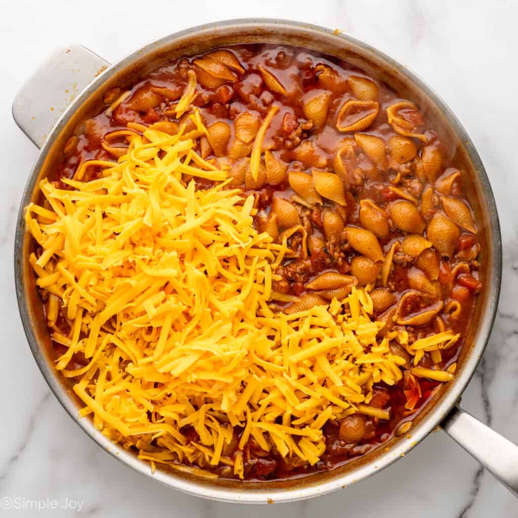 Overhead of skillet of One Pan Cheesy Taco Pasta ingredients with shredded cheese