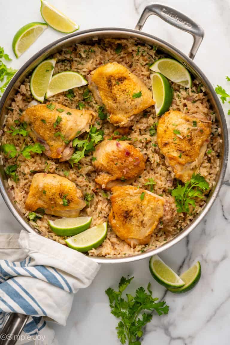 Overhead of skillet of One Pot Coconut Lime Chicken over rice, garnished with fresh cilantro and lime wedges