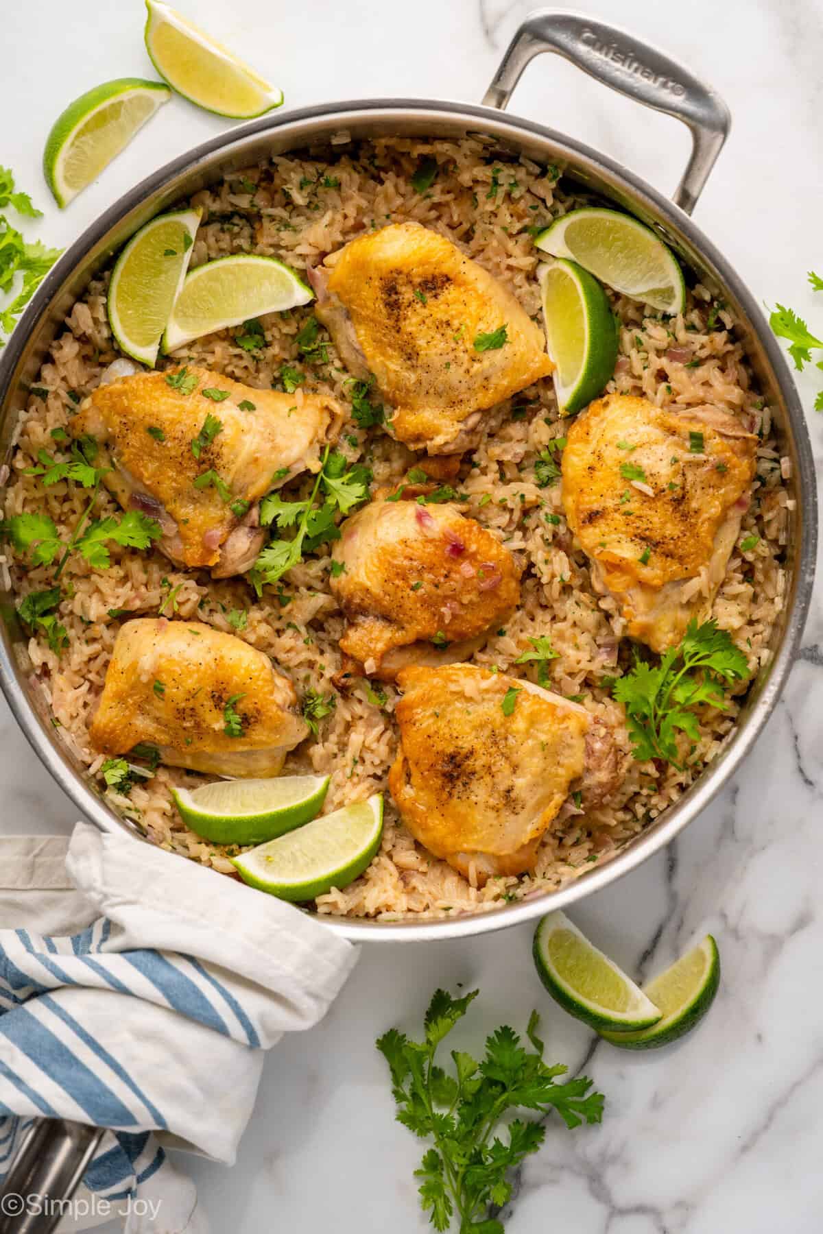 Overhead of skillet of One Pot Coconut Lime Chicken over rice, garnished with fresh cilantro and lime wedges