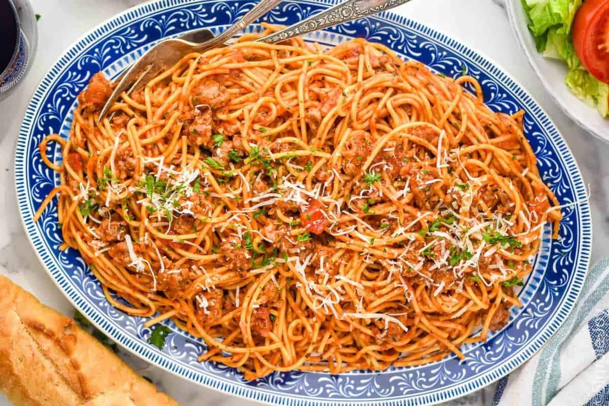 Overhead view of a platter of one pot Sausage Spaghetti with two forks for serving. Bread and bowl of salad beside