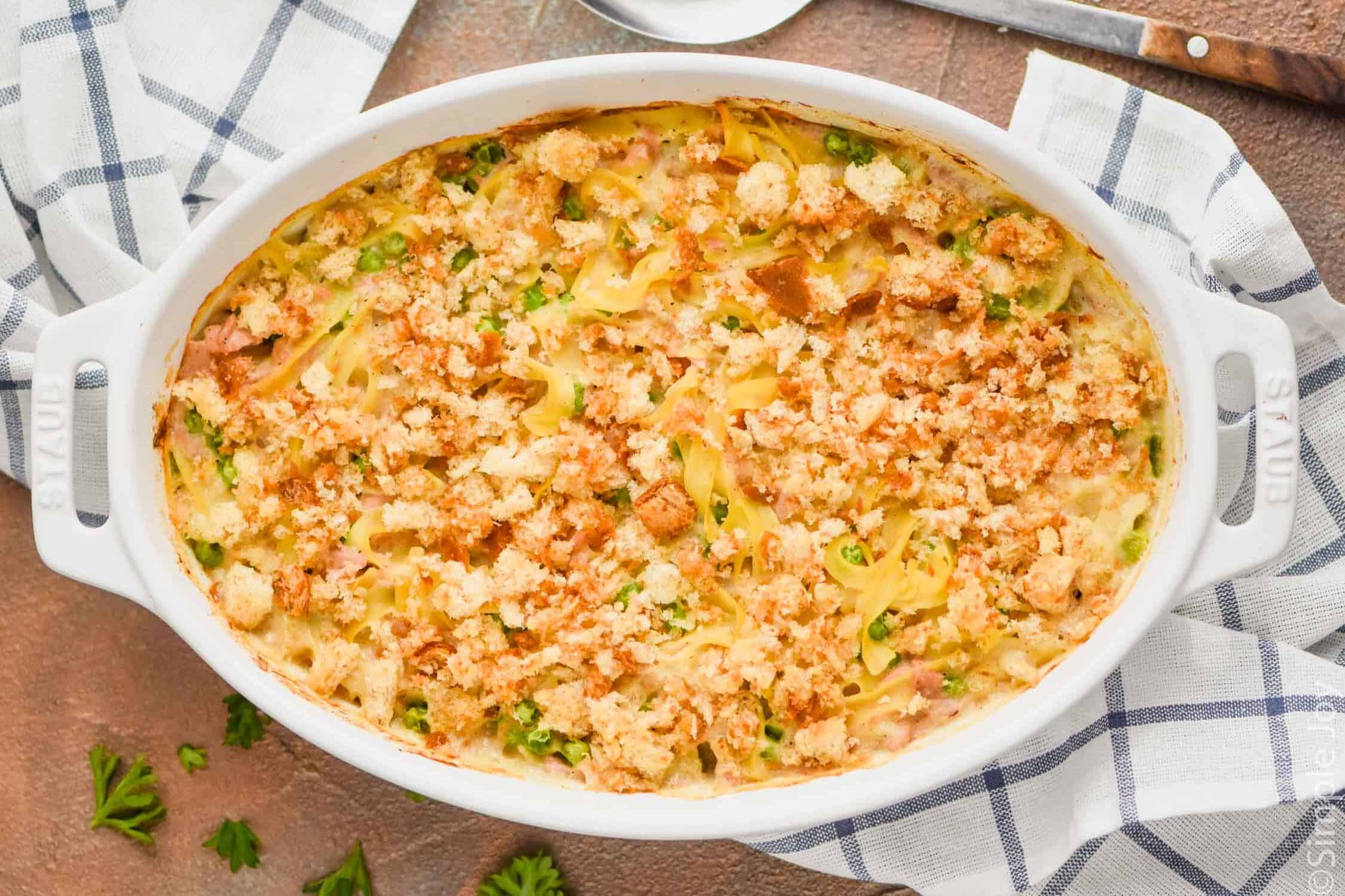 overhead view of oval casserole dish full of tuna casserole and garnished with parsley on a white cloth napkin with blue stripes