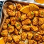 Pinterest graphic for Baked Orange Chicken. Says "30 minute baked orange chicken simplejoy.com" Image shows overhead of baking sheet of Baked Orange Chicken with wooden spoon and orange slices.