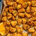 Overhead of baking sheet of Baked Orange Chicken with wooden spoon and orange slices