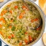 Overhead of large pot of chicken and rice soup with ladle, baguette sitting beside