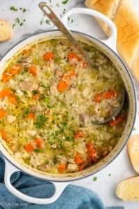 Overhead of large pot of chicken and rice soup with ladle, baguette sitting beside