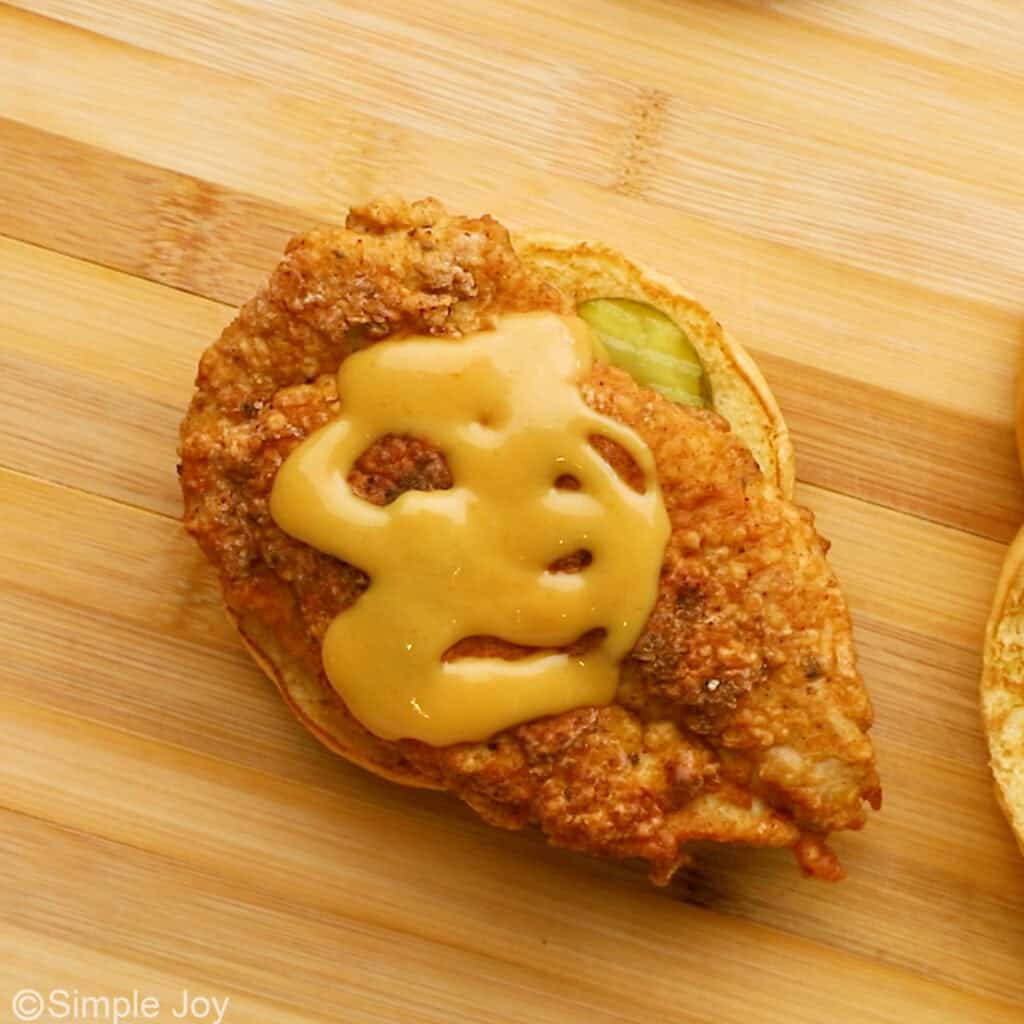 Overhead of bun topped with pickles, breading chicken breast, and chik fil a sauce to make a homemade chicken sandwich