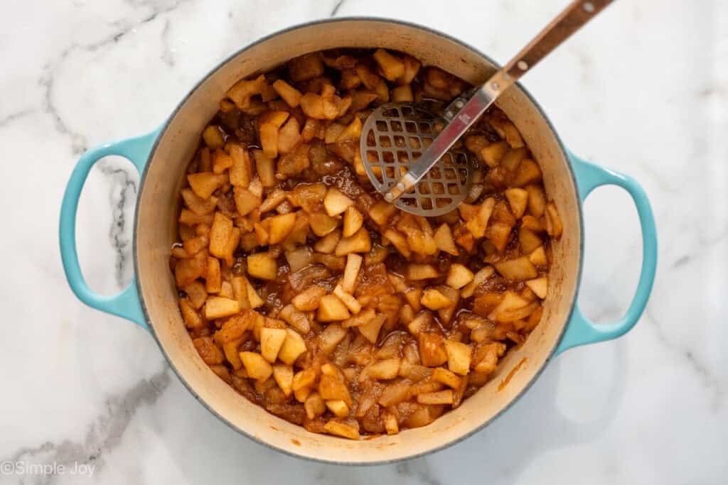 Overhead of large pot of applesauce ingredients with hand masher