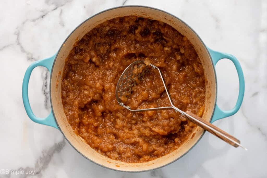 Overhead of large pot of applesauce ingredients with hand masher