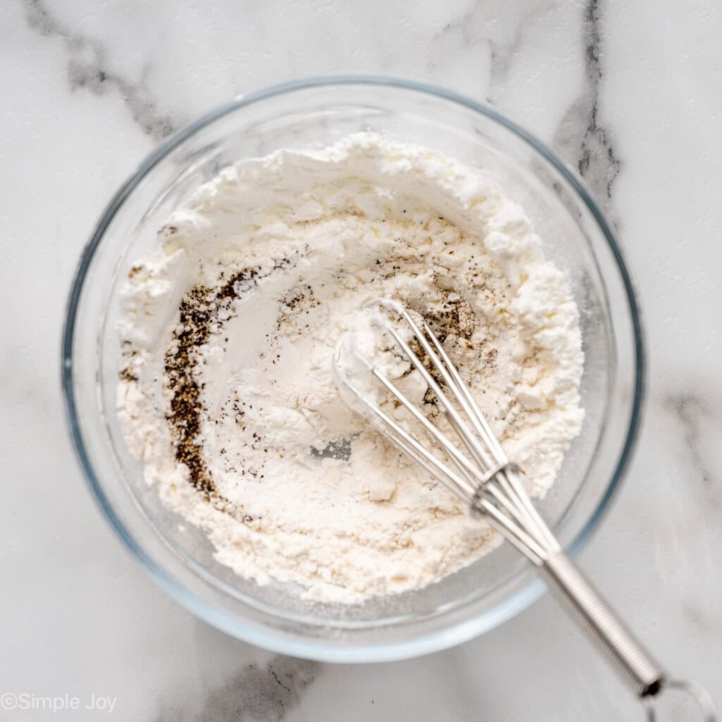 Overhead of glass bowl of flour, spices, and wire whisk to make Baked Orange Chicken