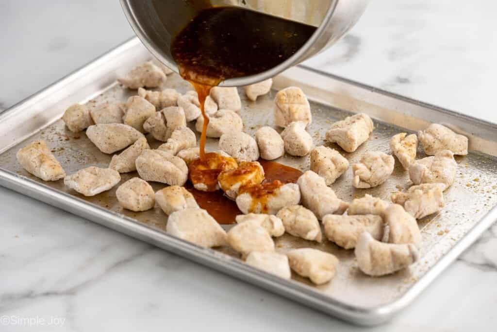 saucepan of orange chickens sauce pouring onto pieces of chicken on a baking sheet to make baked orange chicken