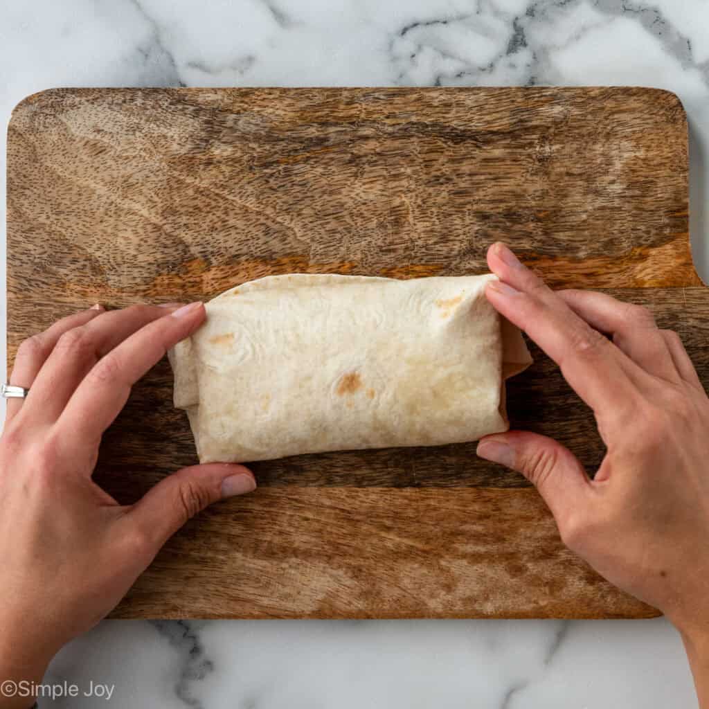 Overhead of person's hands holding a folded breakfast burrito