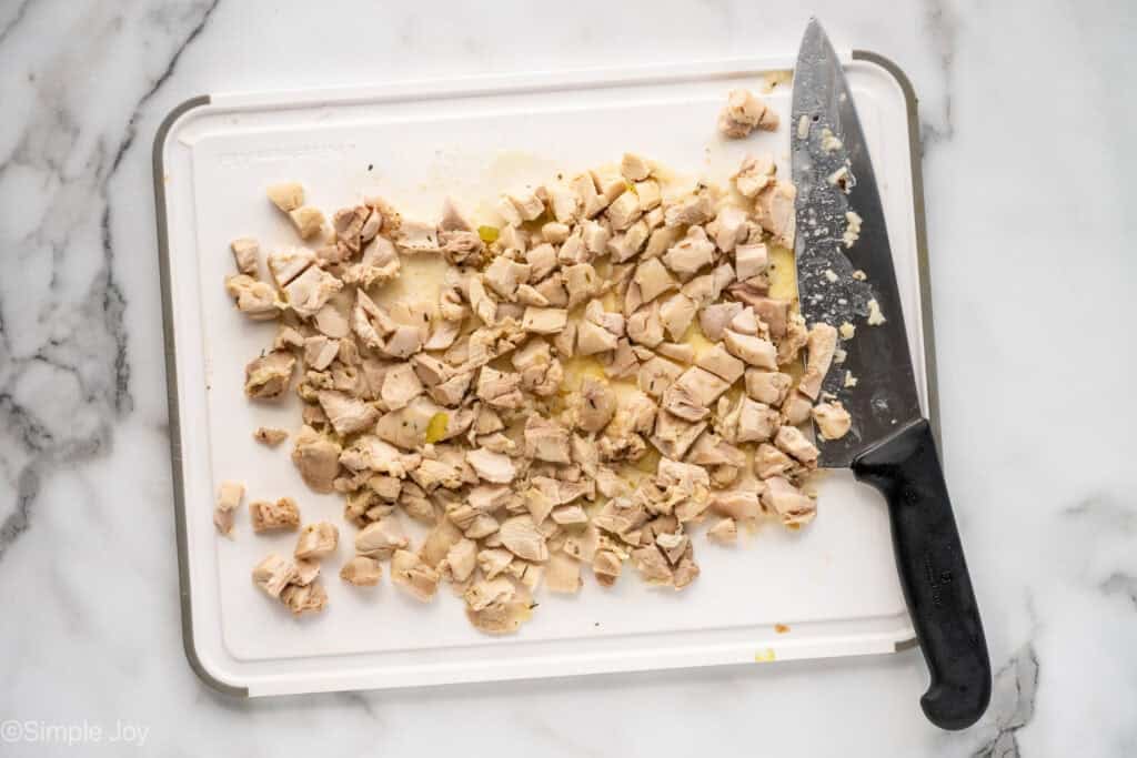 Overhead of diced chicken and large knife on a cutting board to make chicken and rice soup