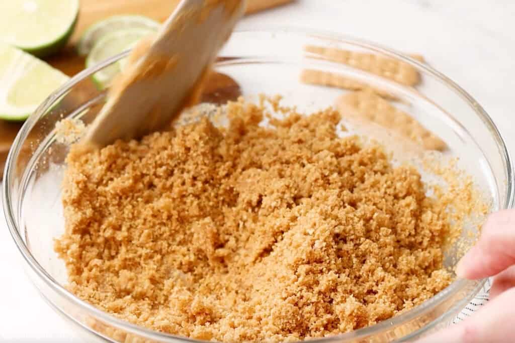 Glass bowl of graham cracker crust ingredients and wooden spoon to make key lime pie recipe