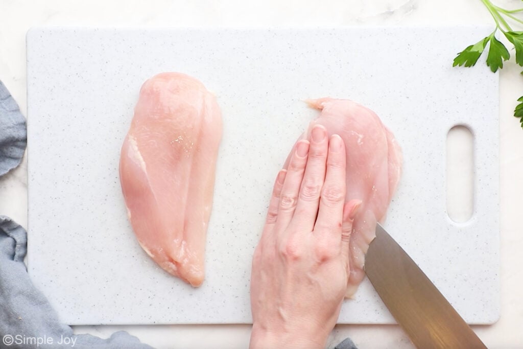 Overhead of person's hand on a chicken breast with knife cutting into it to butterfly it open for parmesan crusted chicken recipe