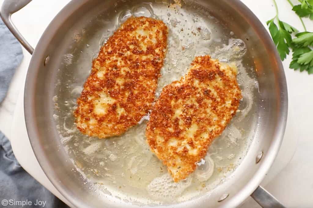 Overhead of parmesan crusted chicken ingredients cooking in a skillet of hot oil