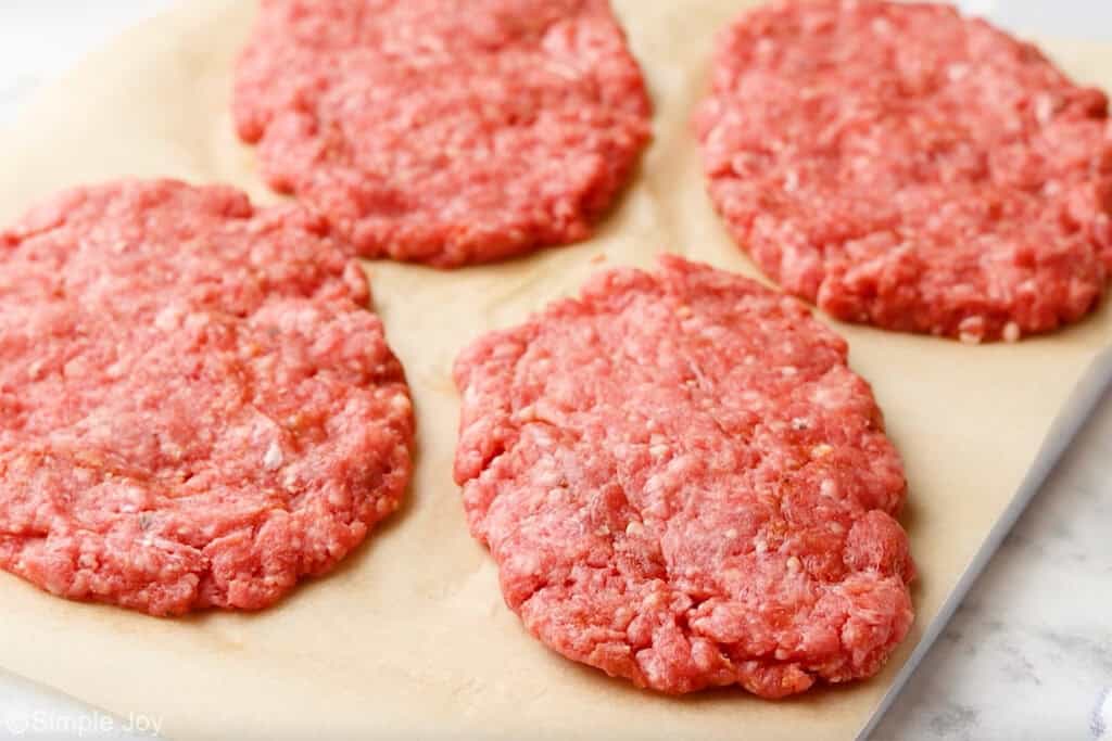4 ground beef patty's on a parchment lined baking sheet to make patty melt recipe