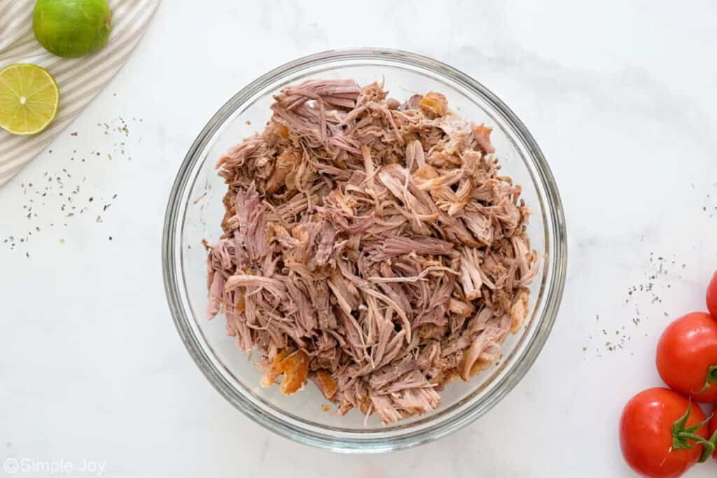 Overhead of glass bowl of shredded pork to make slow cooker carnitas