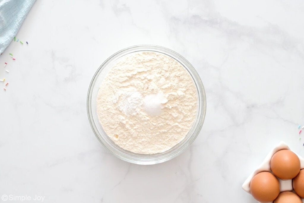 Overhead of glass bowl of sugar cookie ingredients, eggs sitting beside