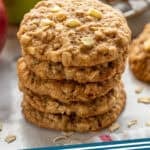 Pinterest graphic for apple cookies. Image shows a stack of apple cookies with apples and cookies on a wire cooling rack in the background. Says "apple cookies simplejoy.com"