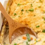 Pinterest graphic for chicken cobbler. Says "crazy easy chicken cobbler simplejoy.com" Image shows a wooden spoon scooping chicken cobbler out of casserole dish