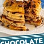 Pinterest graphic for chocolate chip pancakes. Image shows a stack of chocolate chip pancakes topped with butter and syrup. Two mugs of coffee and bowl of strawberries in background. Says "chocolate chip pancakes simplejoy.com"