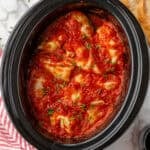 Overhead of slow cooker of cabbage rolls topped with sauce and fresh parsley