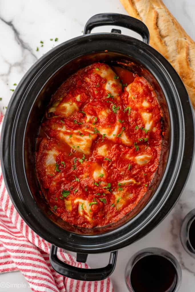 Overhead of slow cooker of cabbage rolls topped with sauce and fresh parsley