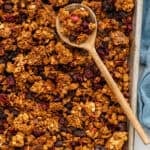 Overhead of baking pan of homemade granola with wooden spoon.
