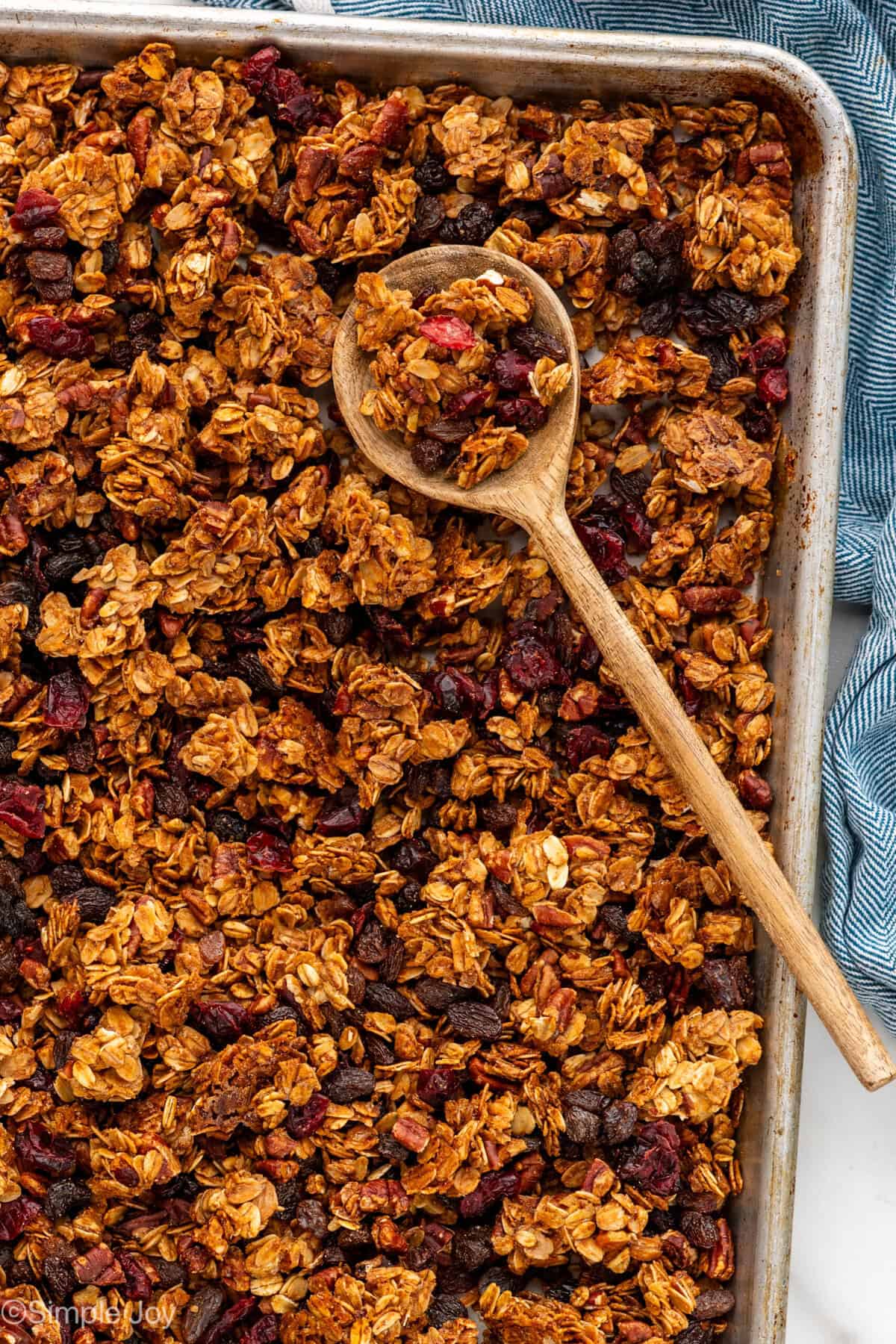 Overhead of baking pan of homemade granola with wooden spoon.