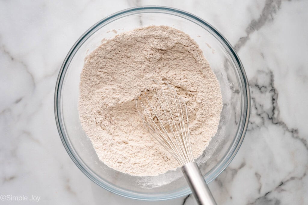 Overhead of glass bowl of apple cookie ingredients with wire whisk