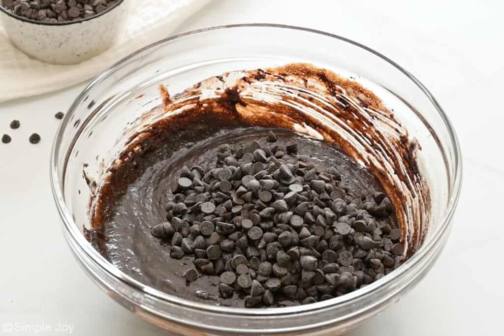Glass bowl of death by chocolate brownies ingredients topped with chocolate chips