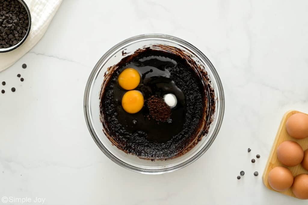 Overhead of glass bowl of death by chocolate brownies ingredients, bowl of chocolate chips and eggs sitting beside