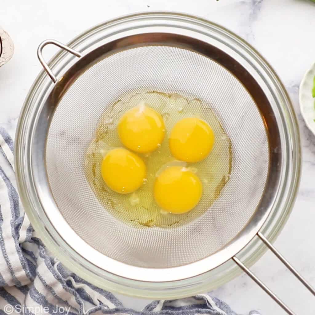 Overhead of four eggs in a metal strainer over a bowl to make egg drop soup recipe