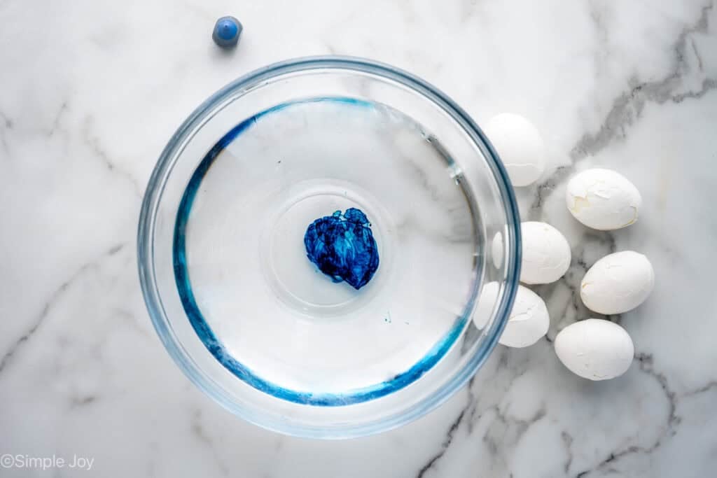 Overhead of glass bowl of water and food coloring with hard boiled eggs sitting beside to make Halloween Deviled Eggs