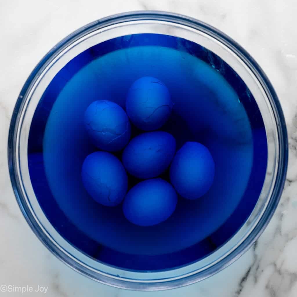 Overhead of glass bowl of hard boiled eggs in blue food coloring to make Halloween Deviled Eggs