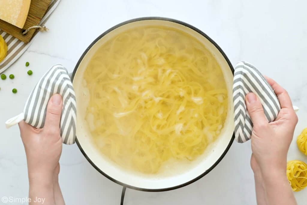 Overhead of person's hands holding pot of pasta in water to make ham and pea pasta