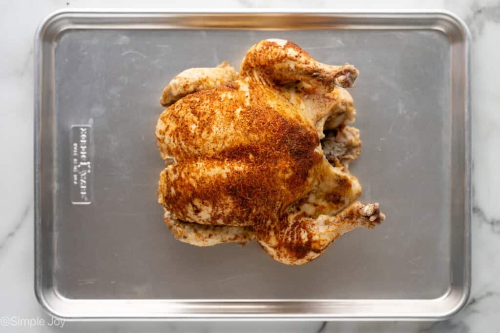 Overhead of whole chicken covered in seasonings on a baking sheet to make Instant Pot Whole Chicken