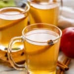 three mugs of crockpot apple cider garnished with a cinnamon stick