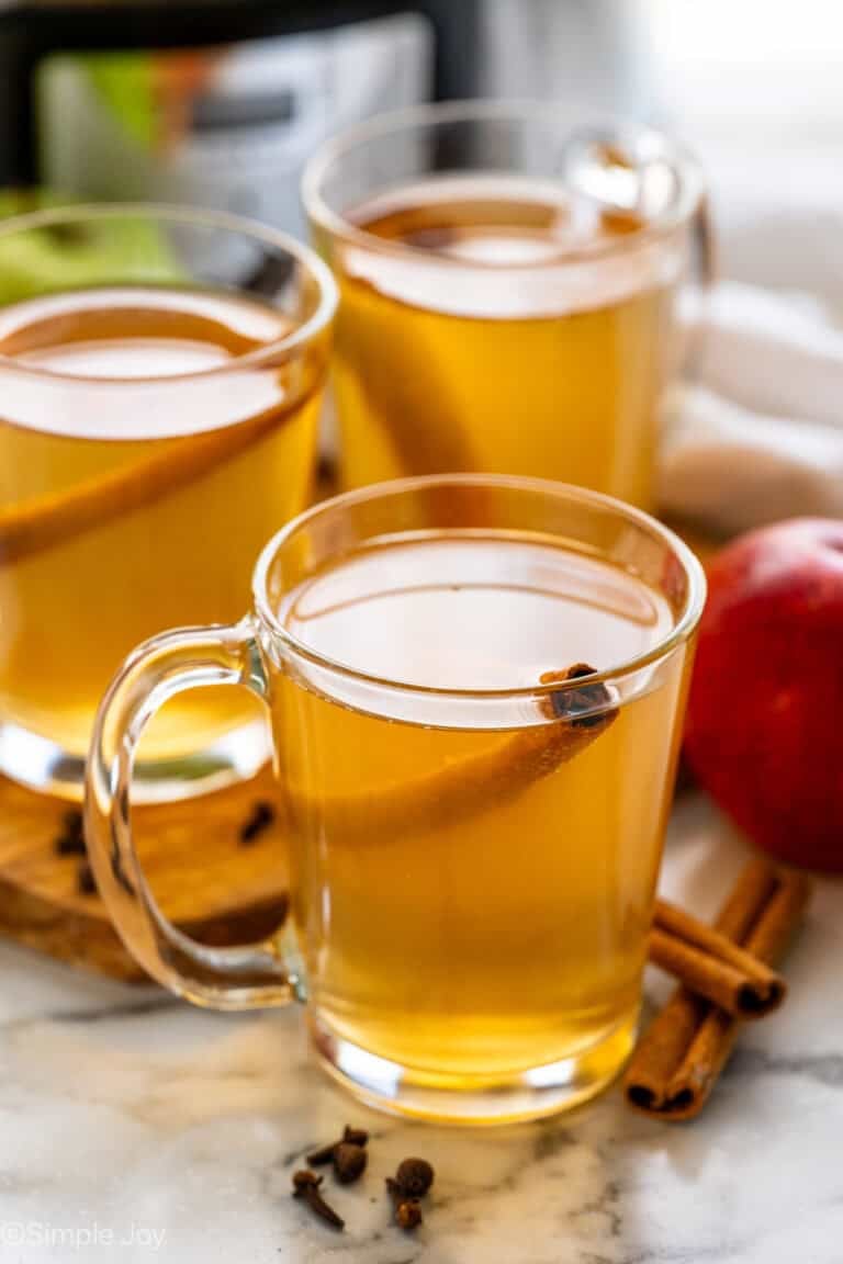 three mugs of crockpot apple cider garnished with a cinnamon stick