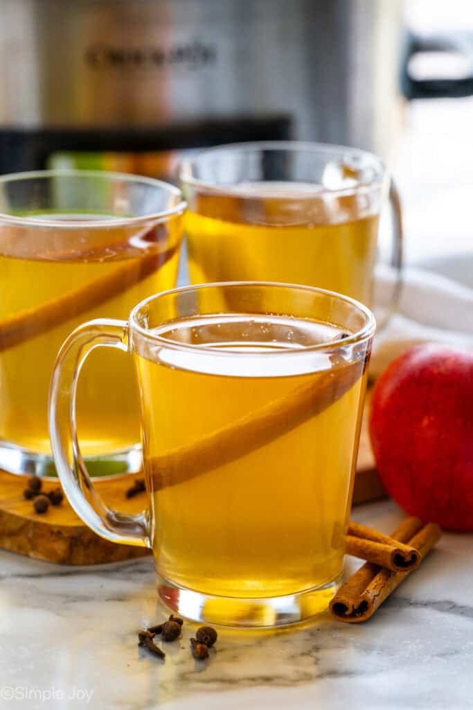 three mugs of crockpot apple cider garnished with a cinnamon stick