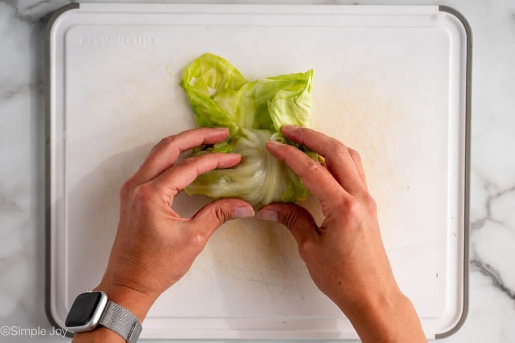 Overhead of woman's hands rolling cabbage leaf with filling to make crockpot cabbage rolls
