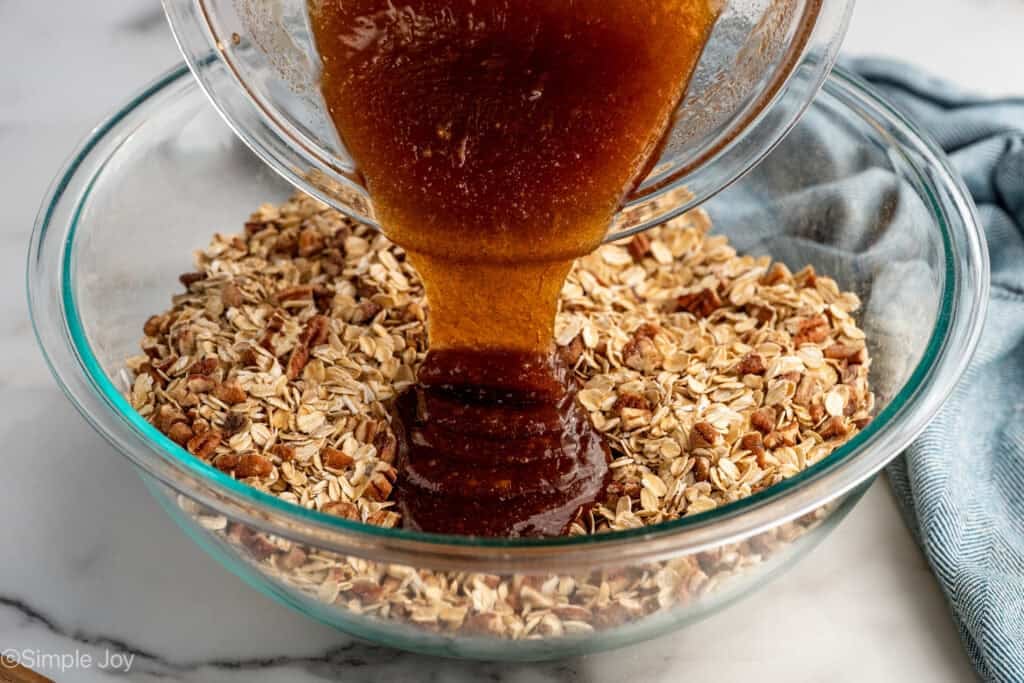 Glass bowl of granola ingredients pouring into another glass bowl granola ingredients
