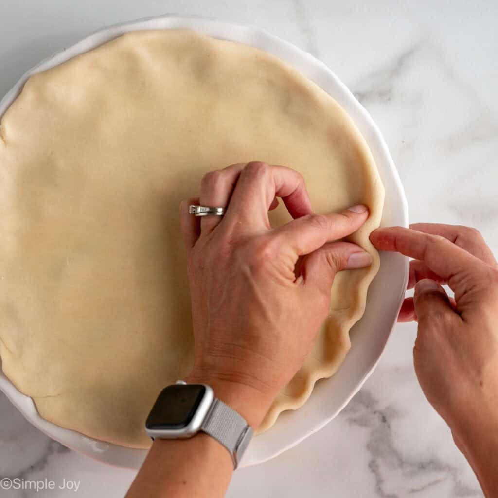 Overhead of woman's hands pinching pie crust on homemade easy chicken pot pie